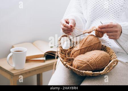 Una donna di mezza età è impegnata in maglieria artigianale domestica, a maglia con fili. Hobby di attività domestico durante il tempo libero Foto Stock