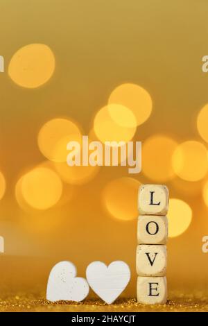 San Valentino. Iscrizione amore fatto di lettere in legno e cuori bianchi su uno sfondo oro glitter con bokeh d'oro. San Valentino sfondo giorno in Foto Stock