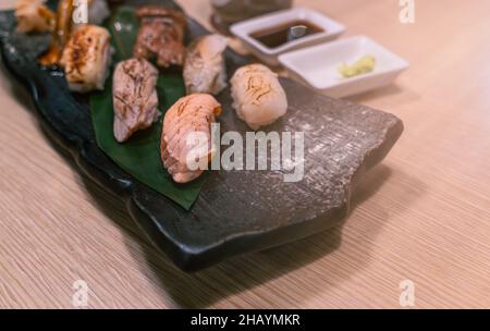 Vari tipi di sushi alla griglia, focalizzazione selezionata sul sushi al salmone alla griglia, viste prospettiche del piatto di pietra nera del sushi mix. Piastra per alimenti sulla linguetta Foto Stock