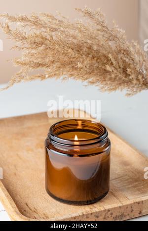 Candela di soia profumata organica in vaso di vetro scuro sul vassoio di bambù minimalismo concetto. Primo piano, spazio di copia per il testo Zero Waste minimalism concetto, mano Foto Stock