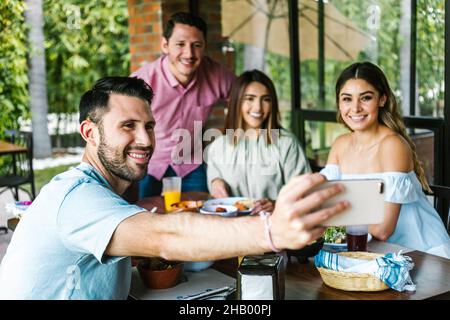 Gruppo di amici latini scattando una foto selfie e mangiando cibo messicano nella terrazza del ristorante in Messico America Latina Foto Stock