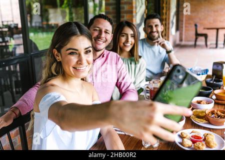 Gruppo di amici latini scattando una foto selfie e mangiando cibo messicano nella terrazza del ristorante in Messico America Latina Foto Stock