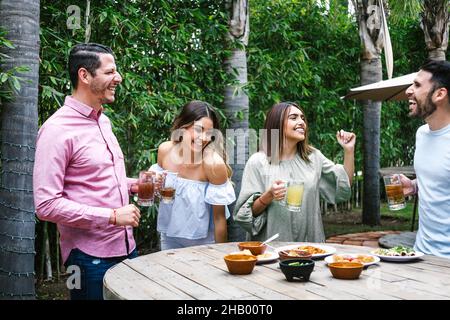 Gruppo di giovani amici latini che si incontrano per birra, bibite michelada e cibo messicano che fa un brindisi nella terrazza del ristorante in Messico America Latina Foto Stock