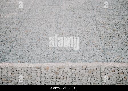 Pietre di granito dietro una griglia di metallo per rinforzare la pendenza. Pietre dietro il filo. Struttura grigia. Costruzione. Foto Stock