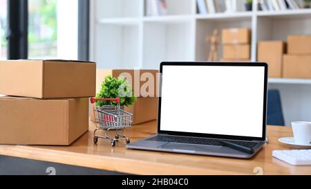 Computer portatile, trolley e scatole di cartone su tavolo di legno. Shopping online o concetto di ecommmerce. Foto Stock