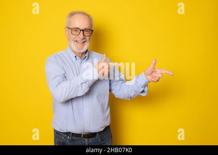 Bell'uomo anziano che indossa una camicia elegante sorridente e guarda la fotocamera puntando con due mani e dita lateralmente. Foto Stock
