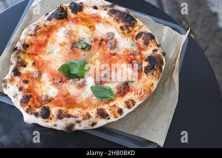 Pizza appena sfornata su vassoio al tavolo nel ristorante all'aperto. Fast food e cucina italiana Foto Stock