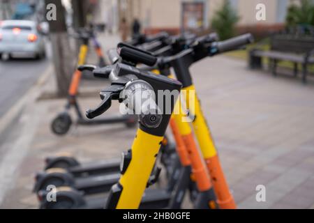 Trasporto urbano elettrico. La fila di biciclette elettriche si prepara a guidare scooter con accumulatori al centro di una città sul marciapiede. Foto Stock