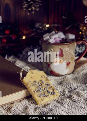 Una fragrante bustina fatta a mano in cera d'api e una tazza con cacao sullo sfondo di un arredamento di Capodanno. Foto Stock