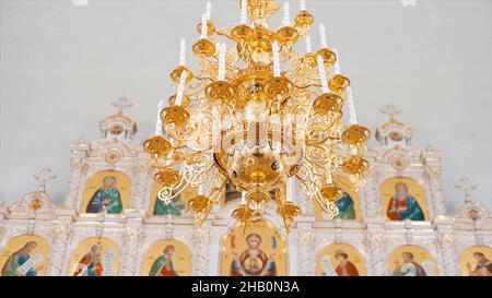 Interno della chiesa ortodossa cristiana in colori bianchi e dorati. Video. Lampadario con candele artificiali nel tempio con iconostasi Foto Stock