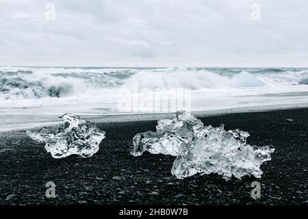 Pezzi di iceberg sulla spiaggia Black Diamond vicino alla laguna di Jokulsarlon, Islanda. Onde dell'oceano Atlantico e cielo nuvoloso sullo sfondo. Fotografia di paesaggio Foto Stock