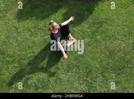 ragazze adolescenti seduti su erba verde in posizione di loto sotto la luce del sole brillante. Occhi chiusi, godere della vita all'aperto. Cute giovane donna rilassa, medita Foto Stock