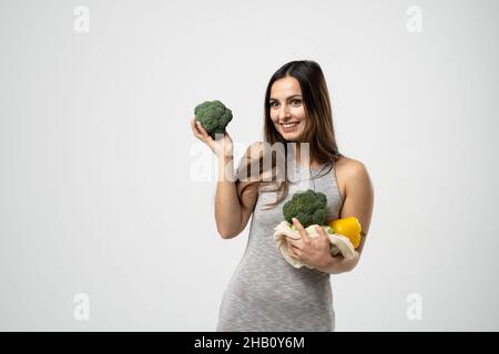 Giovane bruna ragazza tiene le verdure in un sacchetto eco mesh in una mano e un broccoli in un'altra. Concetto di zero rifiuti, shopping ecologico e privo di plastica Foto Stock