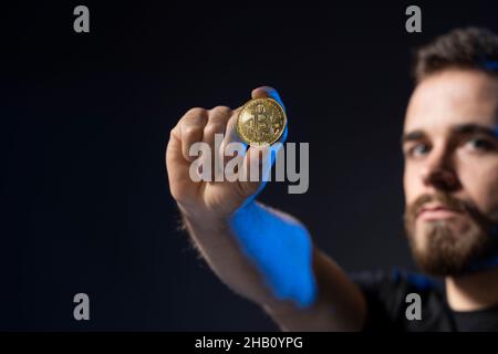 Uomo maturo con bearded indossato in t-shirt nera che tiene in mano il bitcoin d'oro e che sta in piedi isolato su sfondo nero. Foto Stock