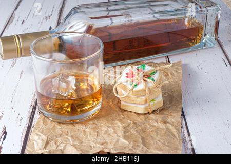 Bicchiere di whiskey con ghiaccio su carta marrone accanto ai biscotti con arco in sisal. Foto Stock