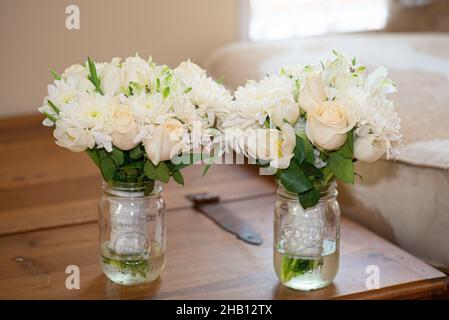 Due rose bianche e rosa e margherite bouquet da sposa in vasetti di mason su tavola di legno Foto Stock
