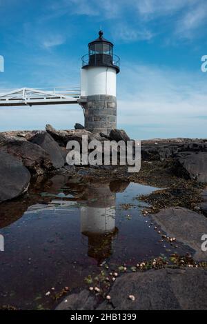 Colpo verticale del faro di Marshall Point riflesso sull'acqua sotto un cielo blu, Maine Foto Stock