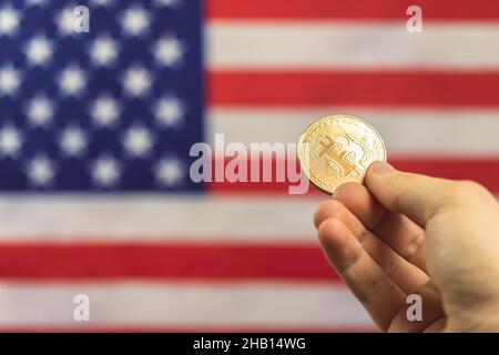 Mano con bitcoin e bandiera USA sullo sfondo. Criptovaluta e concetto degli Stati Uniti d'America Foto Stock