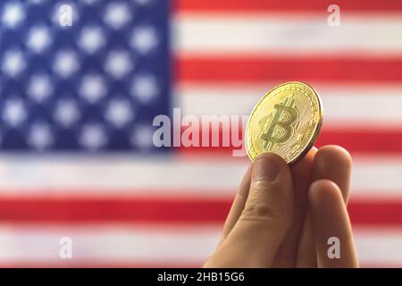 Mano con bitcoin e bandiera USA sullo sfondo. Criptovaluta e concetto degli Stati Uniti d'America Foto Stock