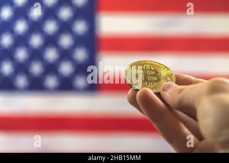 Mano con bitcoin e bandiera USA sullo sfondo. Criptovaluta e concetto degli Stati Uniti d'America Foto Stock