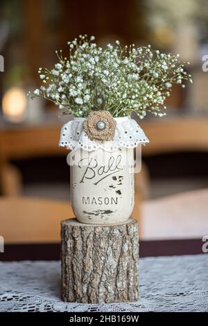 Centrotavola bianca in vaso mason con fiore di tela e i bambini respirano all'interno su un moncone di legno Foto Stock