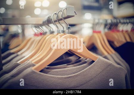 Maglioni su appendiabiti. Shopping in negozio. Abbigliamento su appendiabiti in negozio per la vendita. Sfocatura dello sfondo. Abbigliamento alla moda in una boutique. Abbigliamento vario su m Foto Stock
