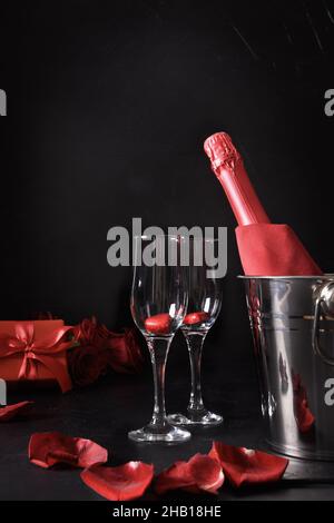 Incontri romantici con flute champagne, regalo, bouquet di rose rosse su sfondo nero. Festa di San Valentino. Formato verticale. Foto Stock