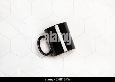 Tazza nera su un piano di lavoro della cucina piastrellato con esagono bianco in una vista dall'alto Foto Stock