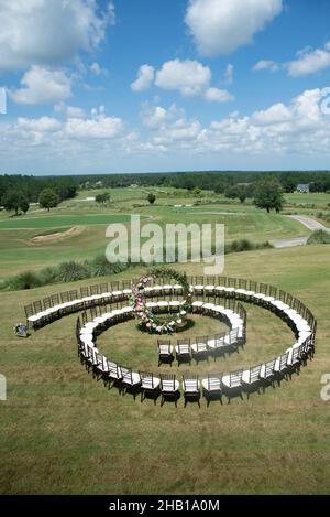 Unica cerimonia nuziale con motivo a spirale, ambientata nella campagna delle colline ondulate, con sedie chiavari marroni e cuscini bianchi Foto Stock