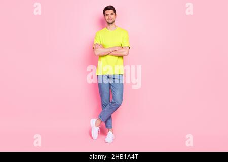 Vista a tutta lunghezza del corpo del ragazzo allegro attraente mani incrociate gambe in piedi isolato su sfondo rosa color pastello Foto Stock