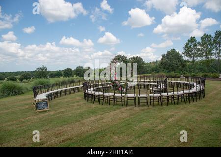 Unica cerimonia nuziale con motivo a spirale, ambientata nella campagna delle colline ondulate, con sedie chiavari marroni e cuscini bianchi Foto Stock