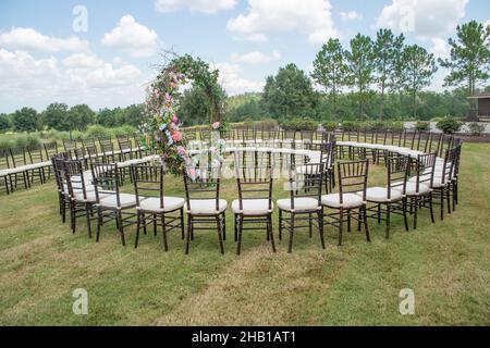 Unica cerimonia nuziale con motivo a spirale, ambientata nella campagna delle colline ondulate, con sedie chiavari marroni e cuscini bianchi Foto Stock