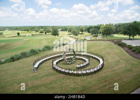 Unica cerimonia nuziale con motivo a spirale, ambientata nella campagna delle colline ondulate, con sedie chiavari marroni e cuscini bianchi Foto Stock