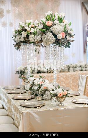 Alti centri per il ricevimento di nozze con cristalli e hydrangee e fiori bianchi e rosa su un tavolo dorato Foto Stock