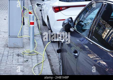 Hannover, Germania - 11 dicembre 2021: Auto elettriche in carica presso la stazione di ricarica pubblica EV durante il parcheggio sulla strada della città. Foto Stock