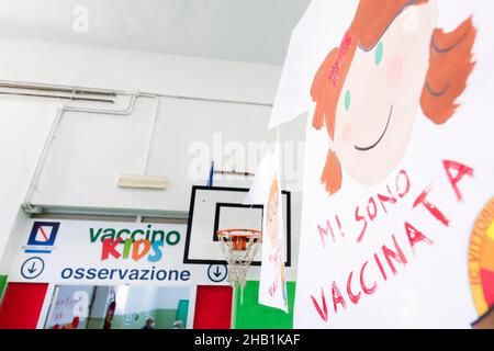 Un segno a forma di T-shirt con un disegno del volto di una bambina e l'iscrizione 'sono vaccinato' (sono stato vaccinato) si trova nella scuola 'Vittorino da Feltre' di San Giovanni a Teduccio, un sobborgo ad est di Napoli, nel sud dell'Italia, Il 16 dicembre 2021. La somministrazione del vaccino pediatrico COVID-19 mRNA Comirnaty (Pfizer) a bambini di età compresa tra 5-11 e 24 anni ha iniziato oggi a proteggere la loro salute e a limitare l'avanzamento del virus. Foto Stock