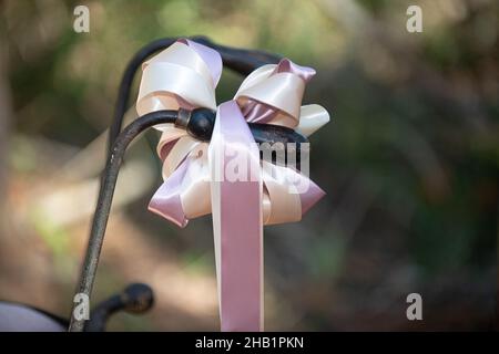 Vecchio cerchio di ruota del carro arrugginito ha parlato attaccato al legno come carrozza del bambino di carrello di ruota di arredamento del cortile con cestino di tessitura dcorated con i fiori rosa e gr Foto Stock