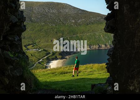 Foto del viaggiatore uomo a Keem Bay Achill Island Irlanda attraverso una finestra di un vecchio edificio Foto Stock