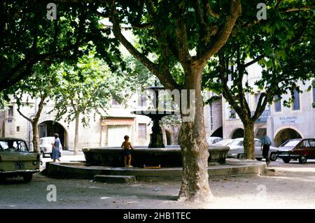 Piccolo ragazzo che gioca da fontana all'ombra di alberi nel centro della città di Uzès, Francia, 1975 Foto Stock