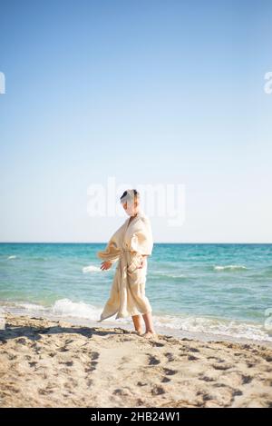 Pratica sulla spiaggia. Un ragazzo in un accappatoio di mussola sullo sfondo del mare sta facendo esercizi di energia. Foto Stock