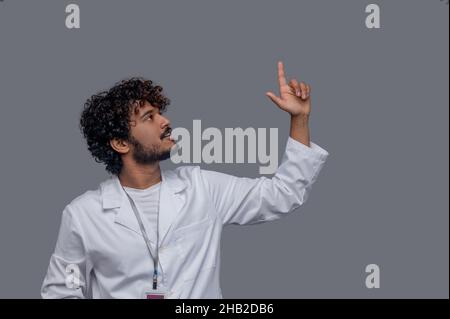 Medico maschio focalizzato con un dito indice sollevato fissando verso l'alto Foto Stock