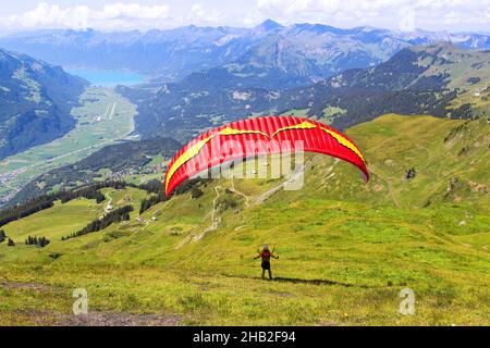 Il parapendio vola sul campo nella zona alpina di Meiringen a Bern Oberland con il lago di Brienz sullo sfondo Foto Stock