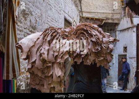 Fez, Marocco - Febbraio 23. 2019: Gente locale che trasporta la pelle grezza sul retro attraverso la stretta corsia in medina (centro storico) al mercato vicino a. Foto Stock