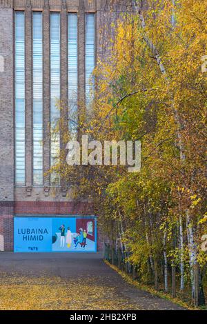 Alberi con colori autunnali e poster banner cartellone pubblicitario Lubaina Himid mostra fuori Tate Modern, Londra UK nel mese di dicembre Foto Stock