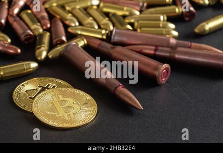 Proiettili in bronzo e ottone sparsi su tavolo nero, monete d'oro bitcoin vicino - uso illegale di criptovaluta per acquistare il concetto di arma Foto Stock