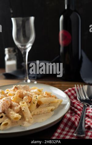 Uno squisito piatto di pasta penne rigate con una deliziosa crema di gamberi e gamberi servita su una tavola STILL LIFE con una bottiglia di vino e un bicchiere nel Foto Stock