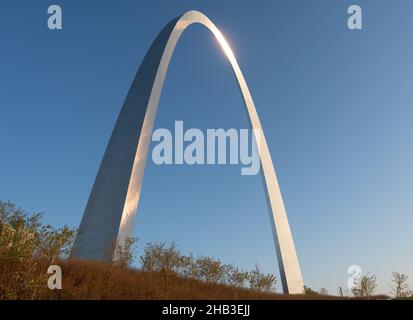 Vista ad angolo basso di St. Louis, il Metal Gateway Arch del Missouri con arbusti, piccoli alberi e erba in primo piano. Fotografato all'alba. Foto Stock
