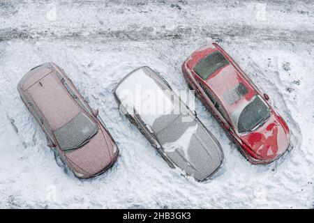 Vista dall'alto del parcheggio dell'edificio degli uffici degli appartamenti con molte auto coperte di neve stucchate dopo una giornata invernale di neve molto frizzante. Rondate di neve Foto Stock