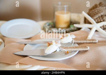 Torta di whimsicle che serve utensili decorati con conchiglie, stelle marine e manico avvolto in twinw al tavolo da torta di nozze Foto Stock