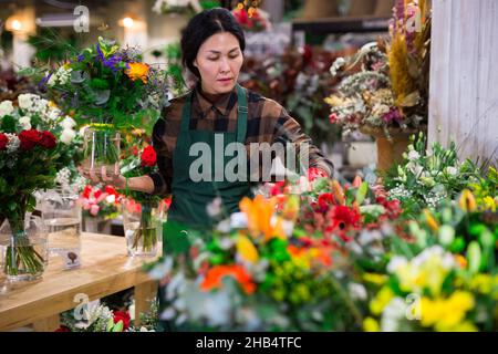 Fiorista femminile asiatico esamina i mazzi in un negozio di fiori Foto Stock